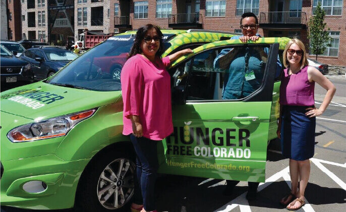 Group of people stand in front of a green car with 'Hunger Free Colorado' on the side