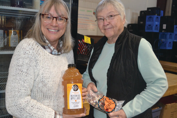 Two people smile into the camera holding apple sauce and carrots - Food pantry