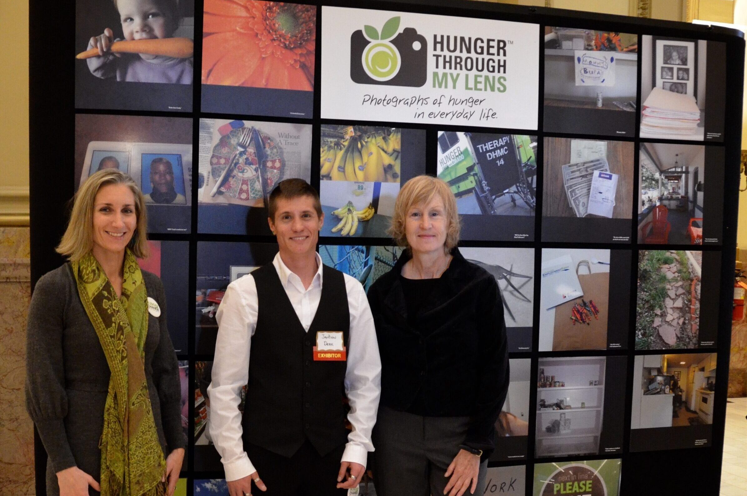 three people standing in front of exhibit of hunger through my lens photos
